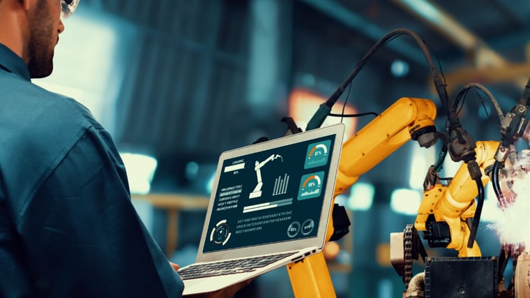 Engineer using laptop to control industrial robot