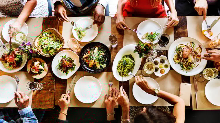 Overhead of an upscale dinner table with healthy dishes and engaged diners.