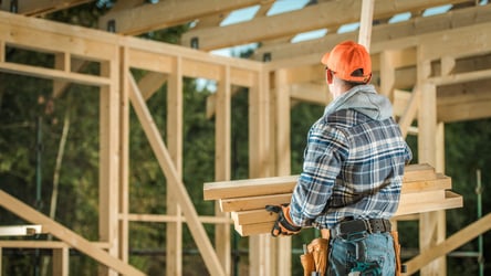 Construction worker holding wood planks inside framed building