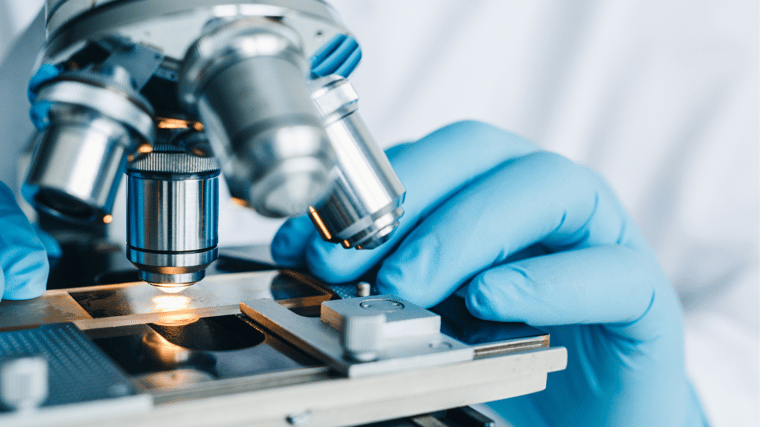 closeup, a medically gloved hand holds a slide under a microscope, healthcare research